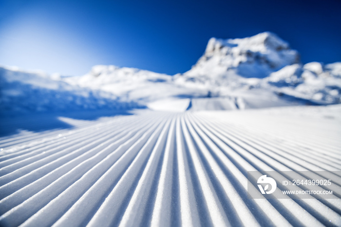 New groomed ski piste or slope. Lines in snow with sunny mountains background. Winter skis concept.