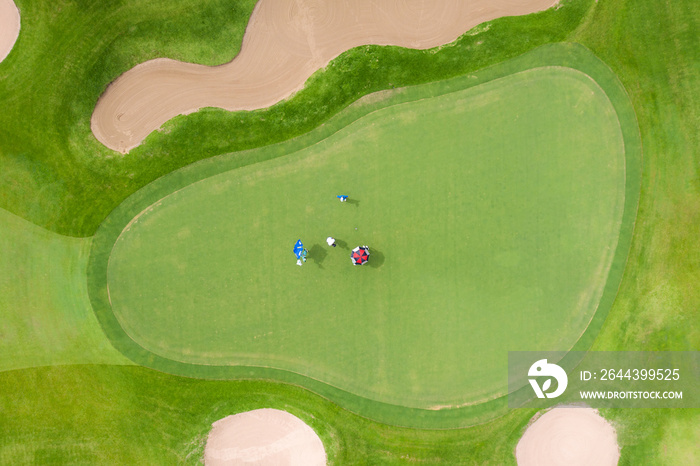 Aerial view of players on a green golf course. Golfer playing on putting green on a summer day.