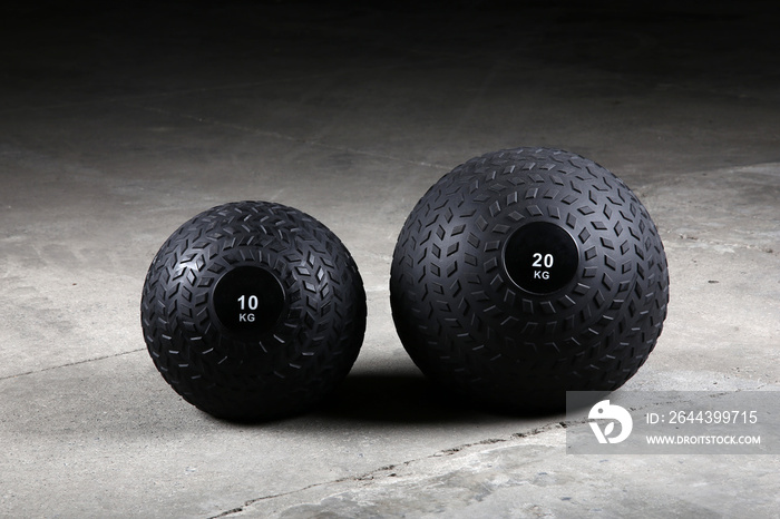 Weighted slam balls at gym on the ground, with nobody. Dark background.