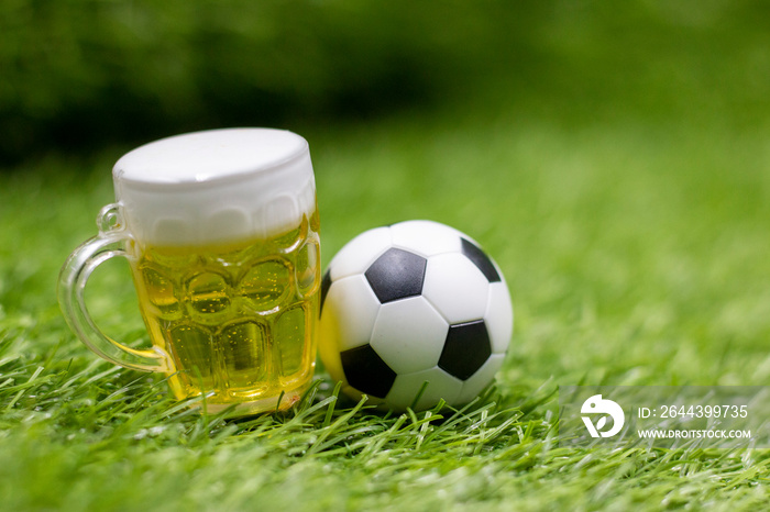 Soccer ball and beer are on green grass