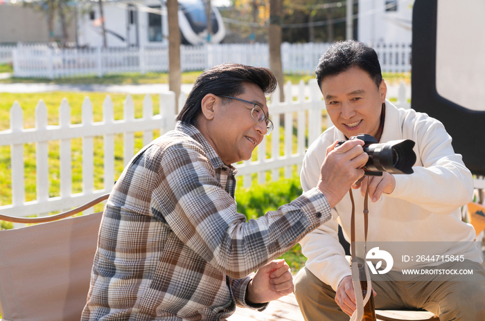 两个老年男人坐在露营地看数码相机