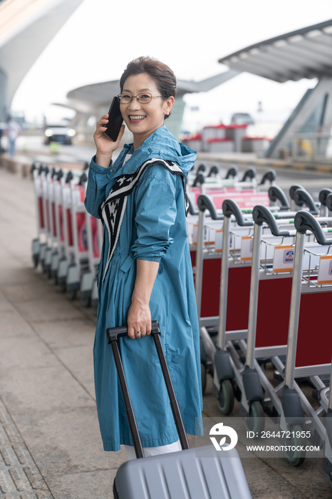 老年女人在机场拉着行李箱打电话