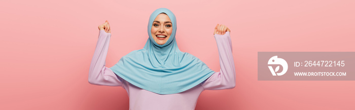 cheerful muslim woman showing yeah gesture on pink background, banner