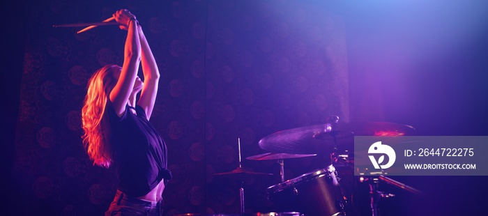 Female drummer playing drum kit on illuminated stage