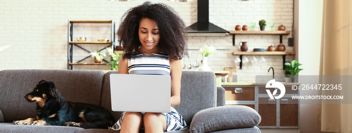 Beautiful African-American woman with cute dog using laptop at home