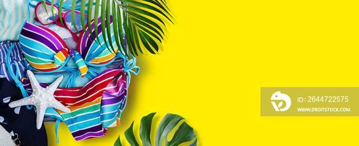 Colorful bikini and clothes in luggage with tropical leaves on yellow background