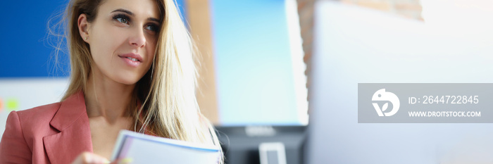 Portrait of business woman with documents in hands looking into computer monitor