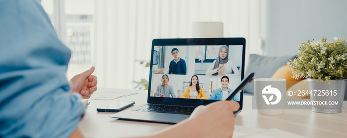 Young Asia businessman using laptop talk to colleagues about plan in video call meeting work from home at living room. Self-isolation, social distance, panoramic banner background with copy space.