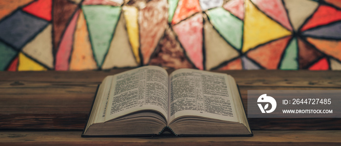 Bible on a old wooden table. Beautiful Stained-glass windows background. Religion concept..