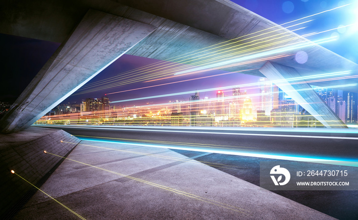 Empty asphalt road under the bridge during the night with light trails and beautiful city skyline background .