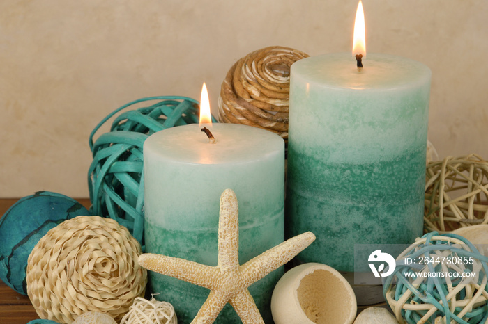 Spa concept with blue and teal colored burning candles arranged on a warm wooden table with beach elements. Starfish and potpourri elements