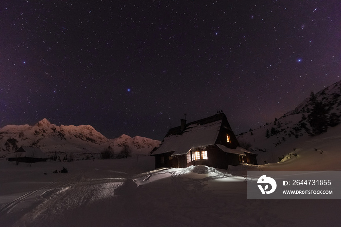 Night winter landscapes in the High Tatras, with mountain houses on a background of snow-capped mountains and starry sky