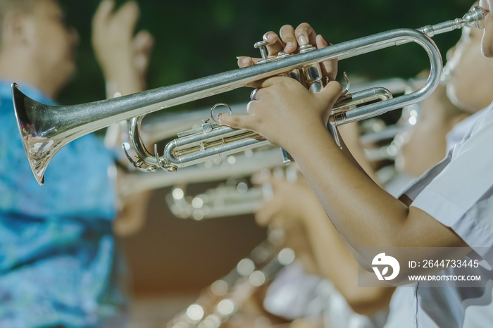 Male student with friends blow the trumpet with the band for performance on stage at night.