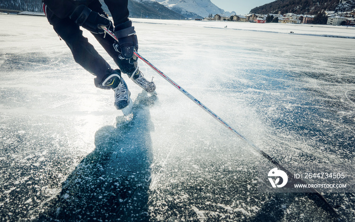 Winter sports ice skating on a sunny day. Ice skating in nature. Scenic panoramic view of the silhouette of a young hockey player skating on a frozen lake. Travel and sports