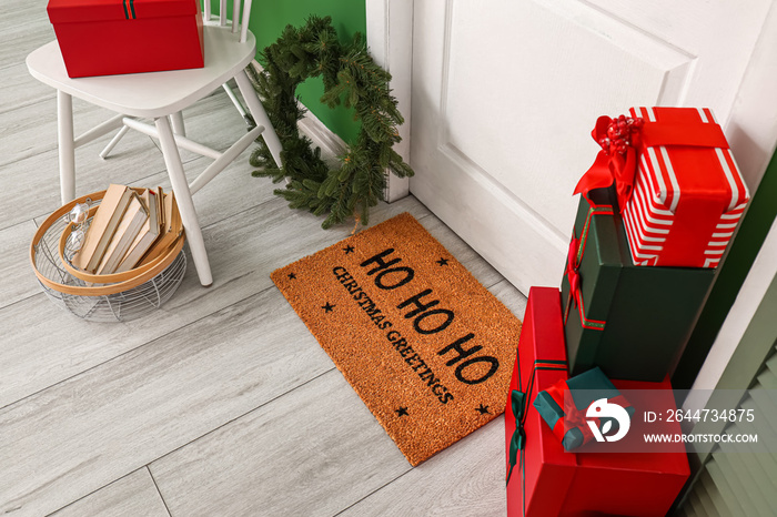 Door mat with Christmas greeting, wreath and gifts in room