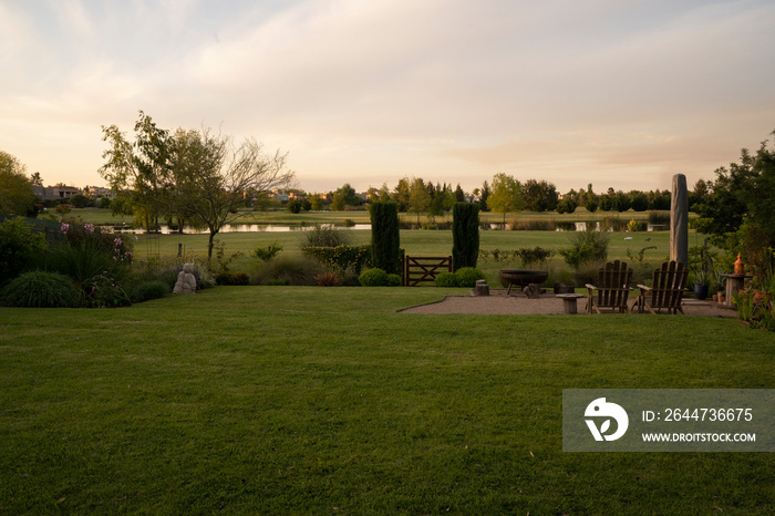 The suburban house backyard at sunset. View of the green grass and lake in the background with beautiful dusk colors.