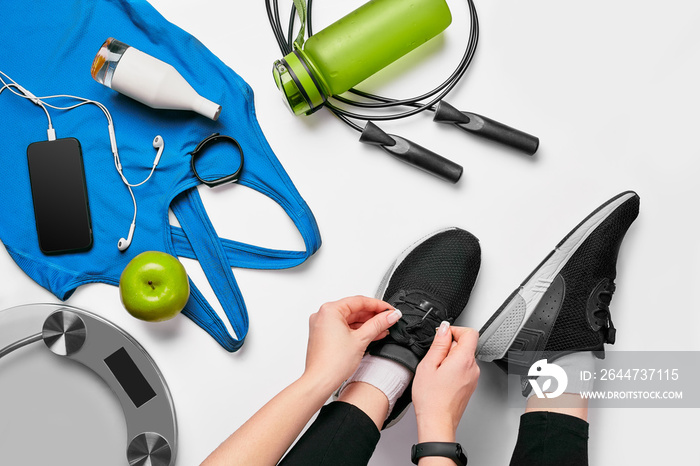 Overhead view of woman hands tying shoes with sport equipments on white background