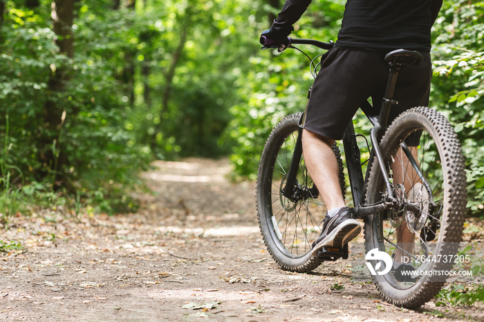 Legs of male cyclist riding bike by forest trail