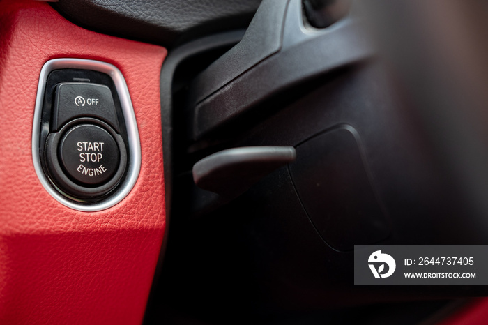 Close-up, isolated image of an engine Start Stop button seen on the dashboard of a german manufactured sports car, also showing its part red leather.