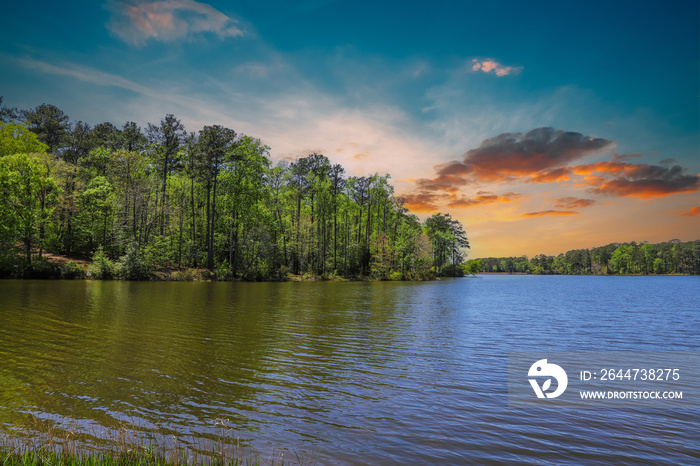 A gorgeous silky green rippling lake surrounded by lush green trees, grass and plants with a gorgeous powerful clouds at sunset at Callaway Gardens in Pine Mountain Georgia USA