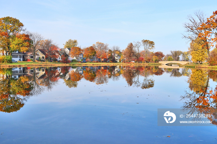 Beautiful fall landscape with a bridge in the city park. Small neighborhood homes around a pond, colored trees and bridge in sunlight reflected in the water. Tenney Park, Madison, Midwest USA, WI