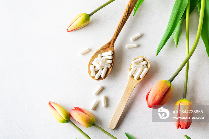 Collagen capsules for skin care and beauty in the wooden spoons on white marble background with beautiful tulip flowers. Health care concept.