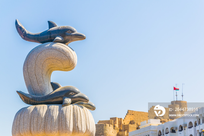 Statue of a dolphin on a Muttrah corniche with a fortress on background, Muscat, Oman.