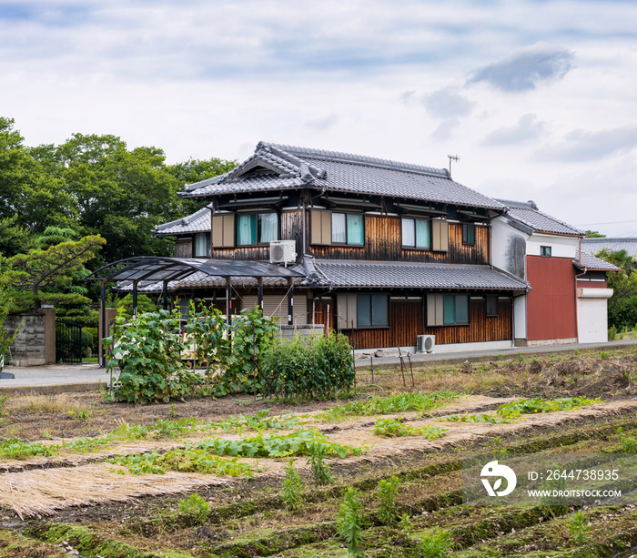 Old Japanese wooden house beside empty farmland and small garden