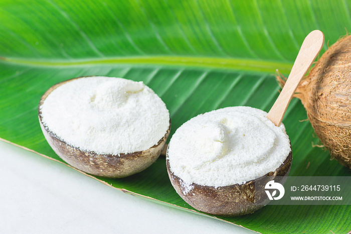 Delicious Vegan Coconut Ice Cream in Bowls with Wooden Spoon on Large Green Palm Tree Leaf on White Marble Table. Plant Based Diet Healthy Dessert Superfood Tropical Vacation Concept