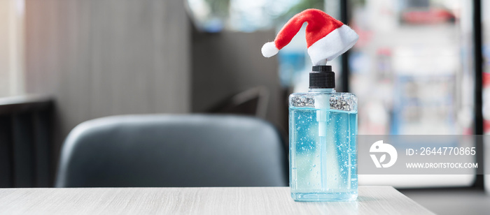 Merry Christmas with Santa Clause hat and wash hand sanitizer gel bottle against coronavirus or Corona Virus Disease (Covid-19) at office Indoor. Holiday, Hygiene, New Normal and Healthcare concept