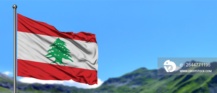 Lebanon flag waving in the blue sky with green fields at mountain peak background. Nature theme.