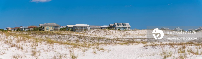 Panorama of dunes with grass near the residences at the beach near Noriego Point in Destin, Florida. There is a vast field of sand slopes at the front near the houses against the sky at the back.