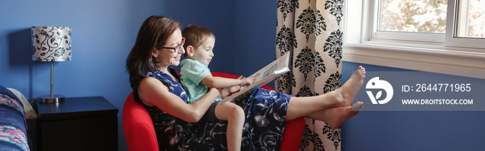 Mother with son boy sitting in armchair and reading book together. Child kid early development literacy. Family mom and baby educational activity. Homeschooling concept. Web banner header.