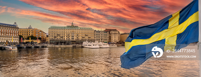 Golden hour panorama of historical Stockholm waterfront at sunset with national flag of Sweden on the first ground.
