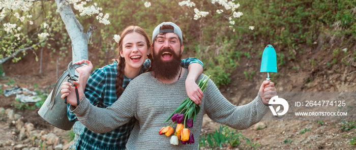 Couple of young farmers in farm, spring banner. Spring couple in love on garden. Loving people in blooming spring garden. Happy couple gardening together outdoor.