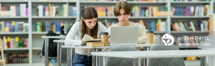 teenage girl reading book near laptop and friend in library, banner.