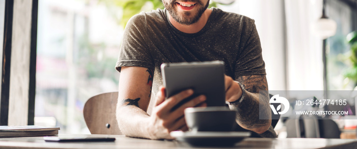 Handsome hipster man relaxing using digital tablet computer and looking at screen relaxing with device work study while sitting on chair in cafe and restaurant.technology and communication concept