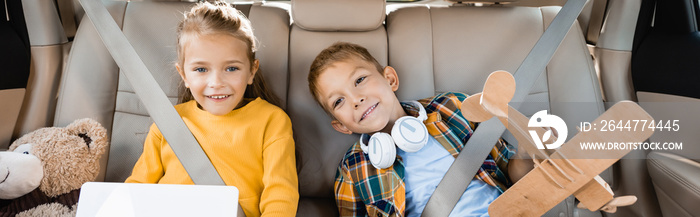 Smiling kids with digital tablet and toys sitting in auto, banner