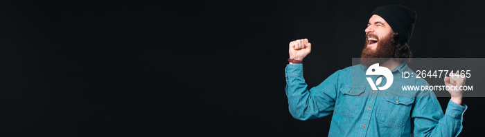 Super excited bearded man is making the winner gesture over black background.