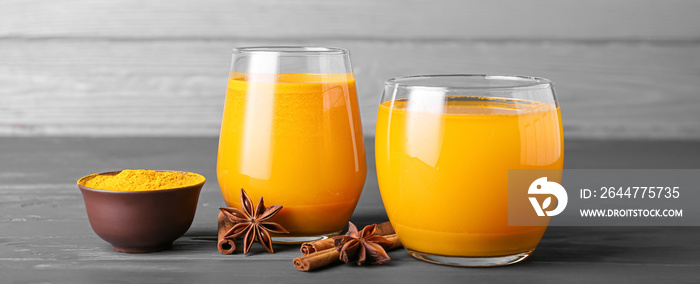 Glasses of healthy turmeric drink on grey wooden background