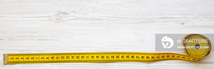 Yellow measuring tape on white wooden table, top view. From above, flat lay. Copy space.