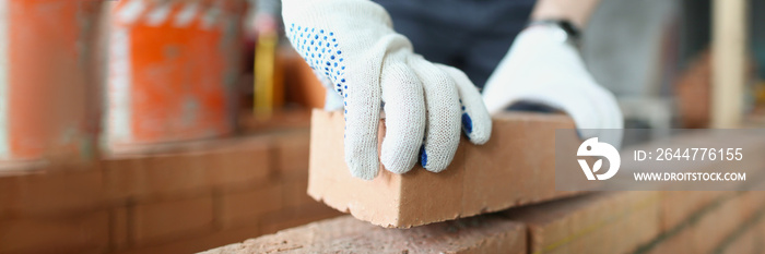 Man builder in protective gloves is building wall of bricks closeup