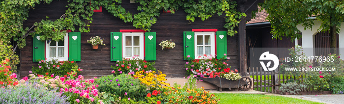 Steirische Holzhausfassade mit Herzchenfensterläden und vielen bunten Blumen