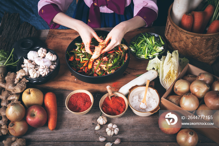 Korean woman is wearing a traditional hanbok, she making Kimchi which is a fermented food preservation of Korean people consisting of many fresh vegetables and fruits, to food concept.