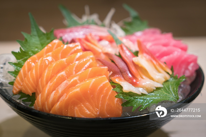 Mixed sliced fish sashimi on ice in black bowl. Sashimi Salmon Tuna Hamachi Prawn and Surf Calm set, raw fish, japanese food in Asian restuarant.