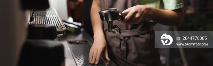 Cropped view of barista holding portafilter near coffee machine in cafe, banner.