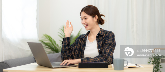 Teenage girl is using laptop to video conference and make greeting gesture with classmates and lecturer after studying e-learning from study remotely at home