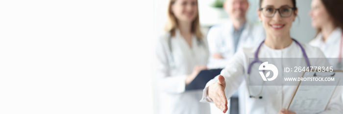 Female doctor stretches out her hand for cooperation against background of medical colleagues