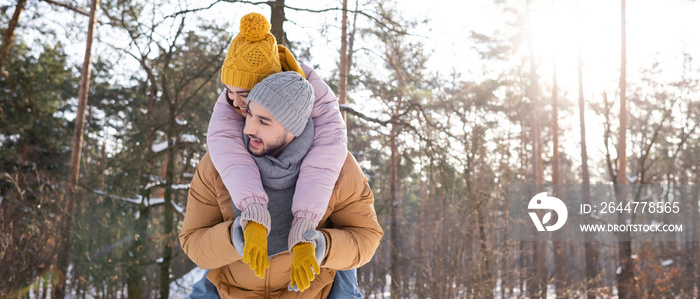 Cheerful woman piggybacking on boyfriend in winter park, banner