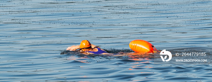 Female swimming in the open water alone wth orange buoy for safety